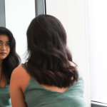 a woman looks at her reflection in a bathroom mirror