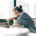 a woman sitting on a couch looking out a window with a book balanced on her lap