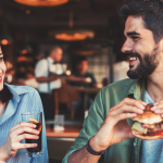 a man and a woman are sitting at a table eating hamburgers and drinking soda
