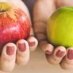 a woman holding a red apple in her left hand and a green apple in her right hand